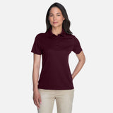Polo pour femme Core365 Performance Origin en marron, vêtement polo, tissu performant, porté par une femme.